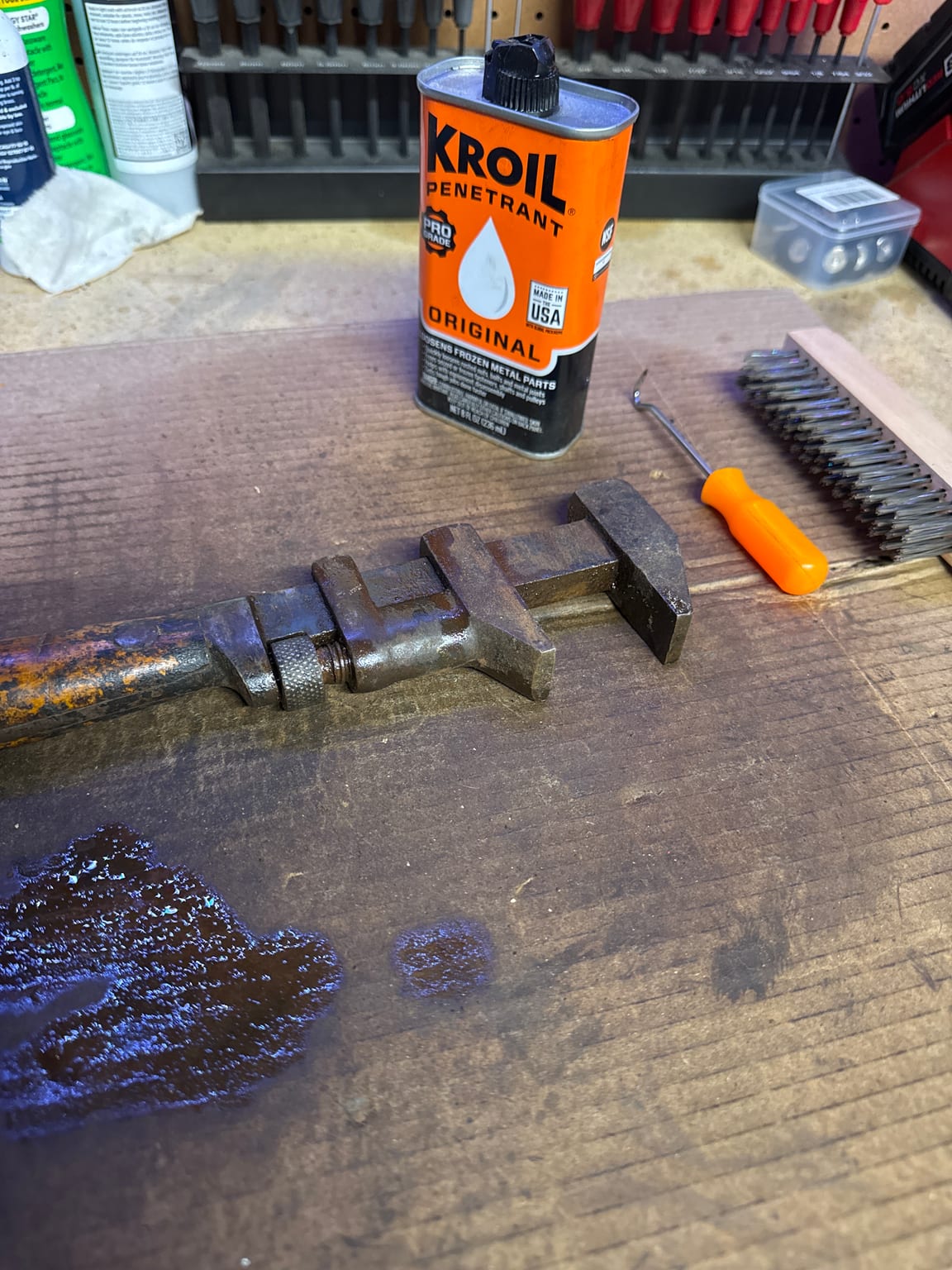 Antique adjustable wrench on a workbench beside a can of Kroil penetrating oil during repair