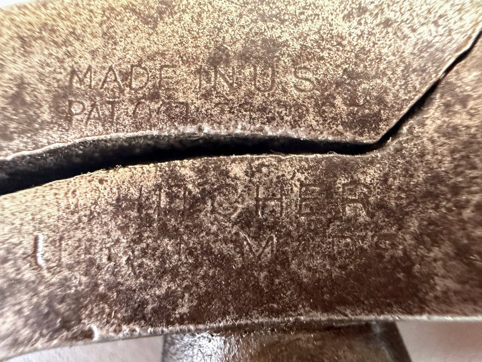 Close photograph of faint markings on antique lasting pliers, including Made in U.S.A., a partial patent date, Whitcher, and Union Made